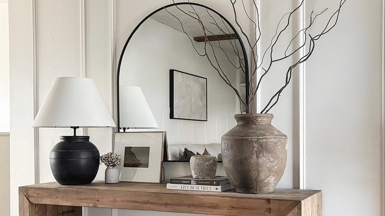 arched mirror on entryway table with layered decor and potted plant