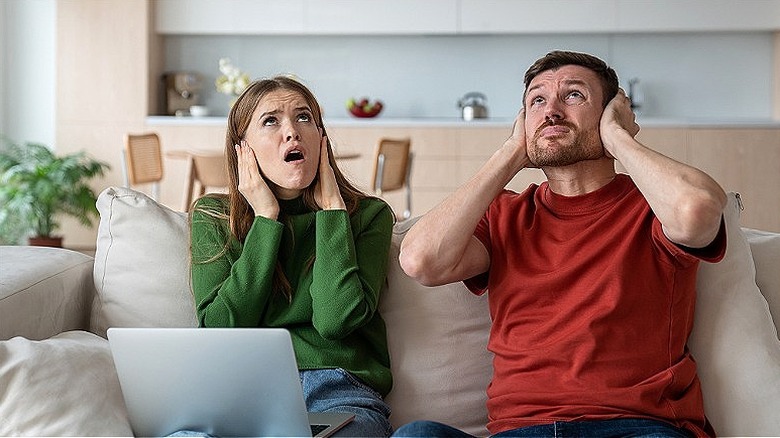 Two people covering their ears and looking up at the ceiling