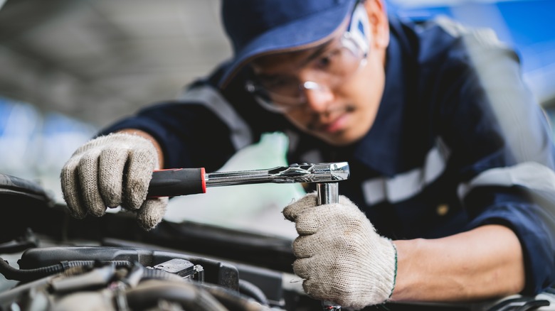 A mechanic with a socket wrench working on an engine