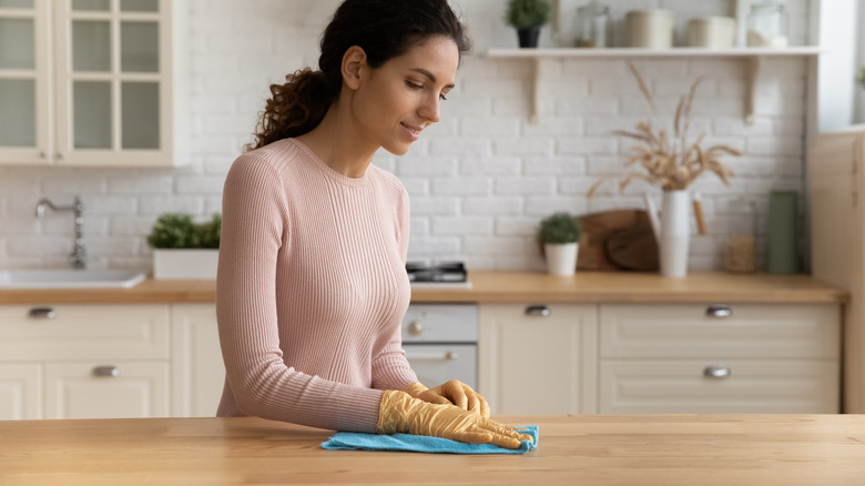 A woman wipes a wooden kitchen countertop using a microfiber cloth