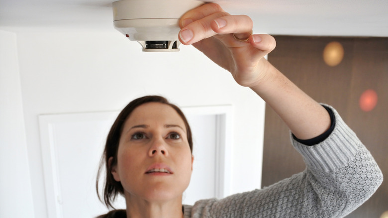 Woman checking smoke detector on ceiling