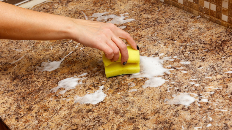 Person cleaning counter with sponge and soapy water