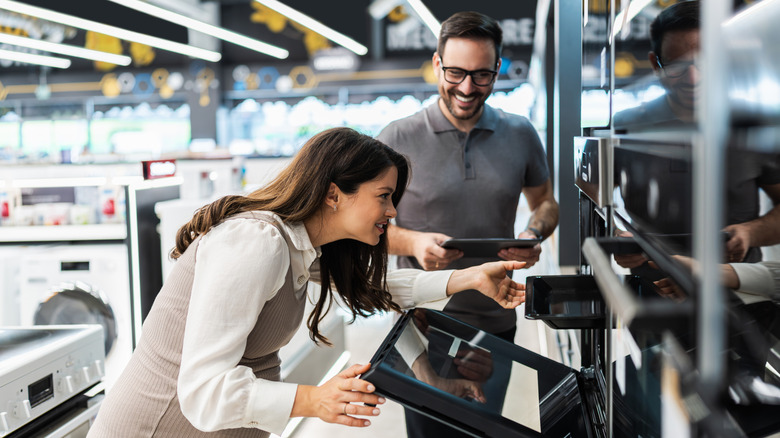 A woman looking into an oven at a store while a salesperson waits with a smile