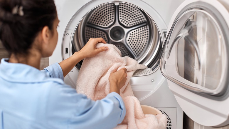 Woman loads pastel pink cotton towel into washing machine