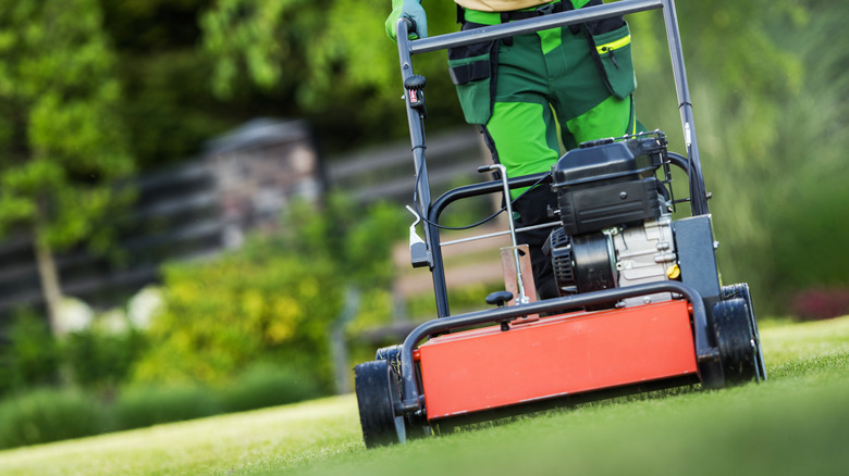Worker in landscaping clothes aerating the lawn