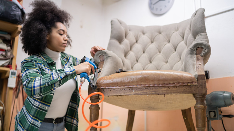 A young woman reupholsters a vintage chair in her shop