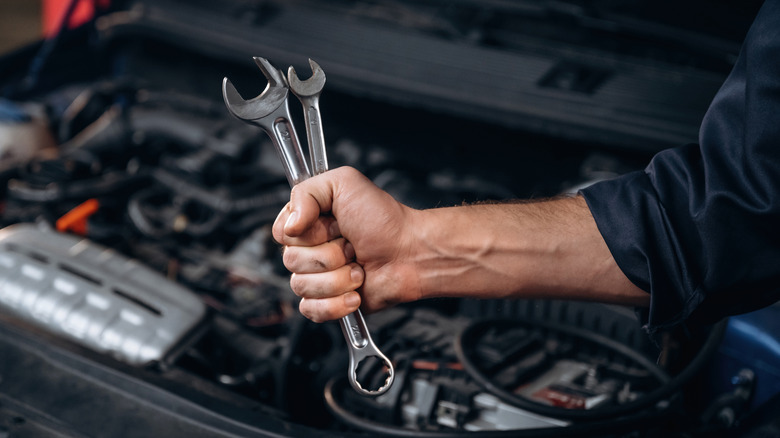A person holding two tools while working on car