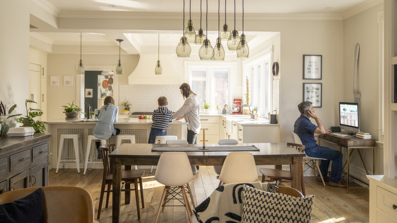 A mother is helping kids with homework on the kitchen island while father works in a corner