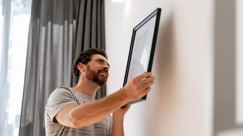 Man hanging a simple white artwork on a wall