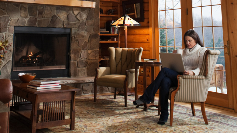 Woman sitting and working on a chair beside a fireplace