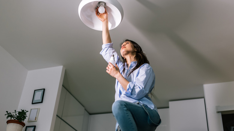 Woman screwing on a bulb in a fixture outside a kitchen