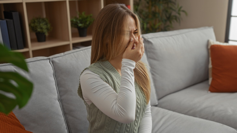 Woman sitting on a sofa and pressing her nostrils closed