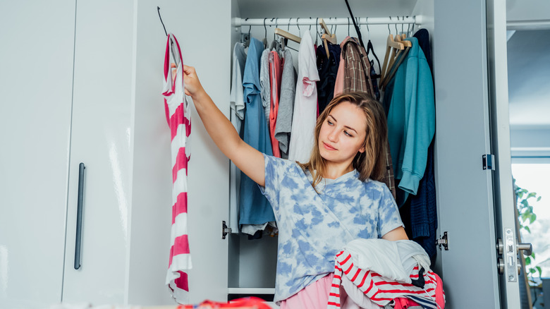 Woman stands in front of her closet, sorting through her clothes.
