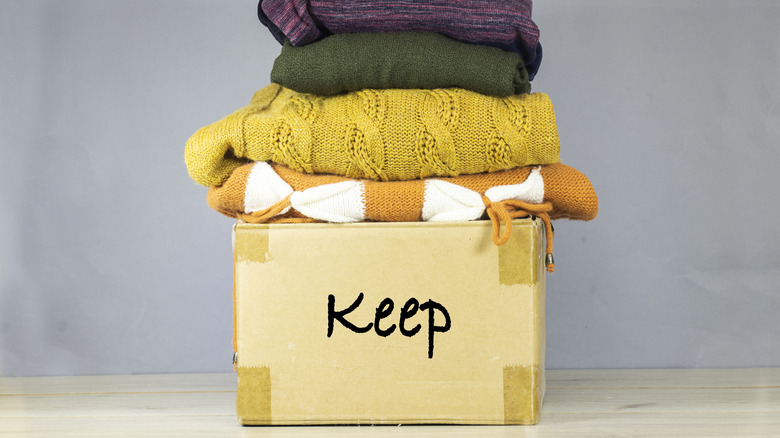 A cardboard box labeled "Keep" and stacked high with sweaters