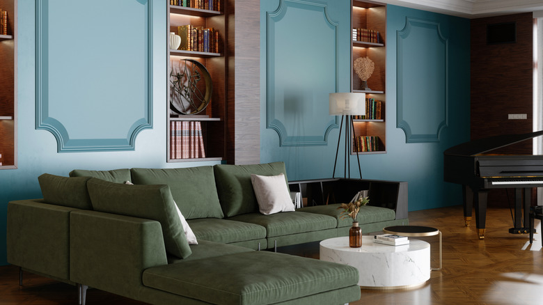 Moody living room with teal walls and dark teal moldings surrounding green velvet couch