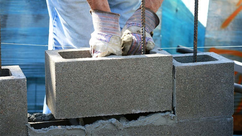 A person wearing gloves, picking up a concrete block by the beam in the middle