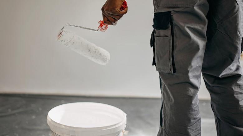 A person holding a paint roller above a paint can