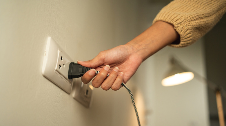 A hand is plugging a power cable into the wall outlet.