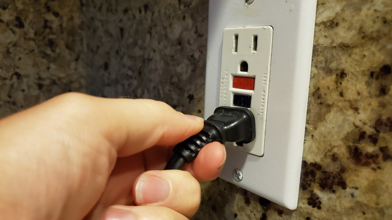 Person plugging something into a GFCI outlet with red and black buttons