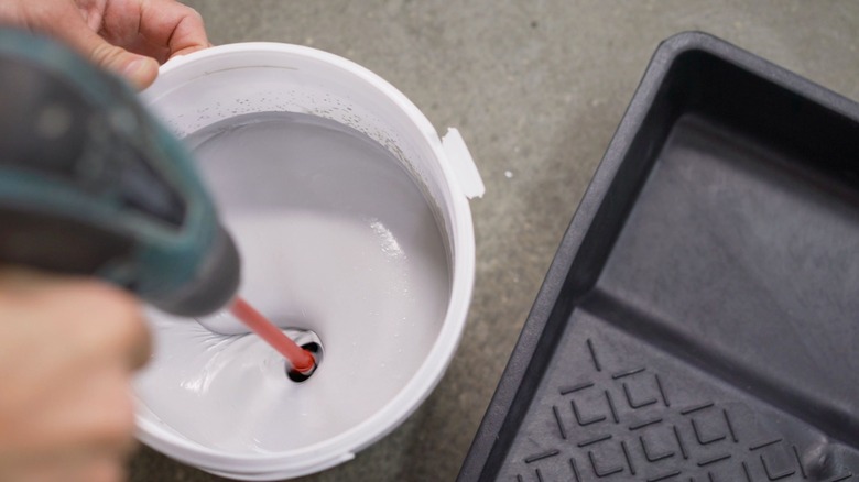 Someone mixing white paint next to a black paint tray