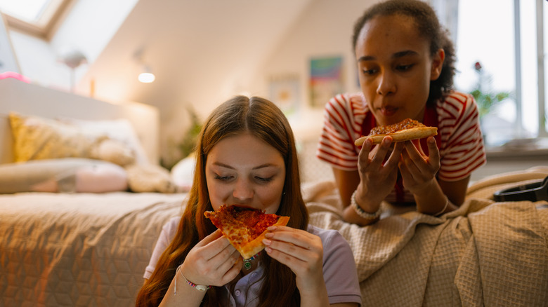 Two girls eating pizza in bed
