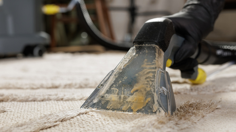 Detail of gloved worker using extraction nozzle to pull dirty solution from beige carpet surface