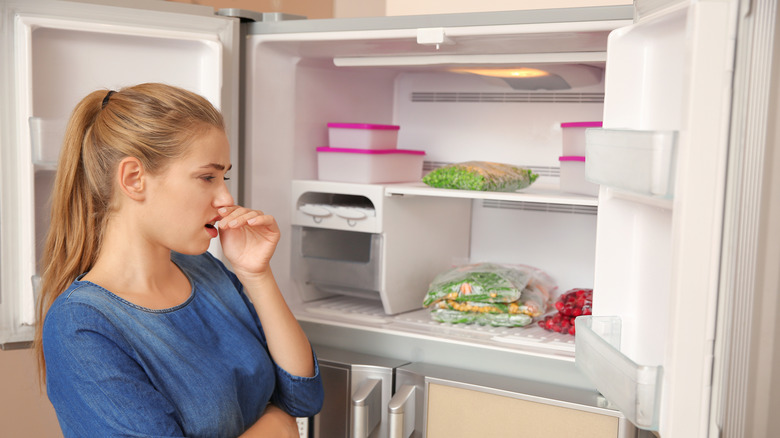 Woman holding nose due to putrid odor from freezer