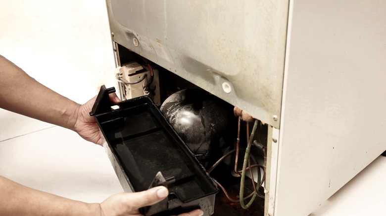 Hand taking out a black drip tray from a fridge