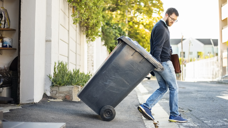 person wheeling trash bin out of garage