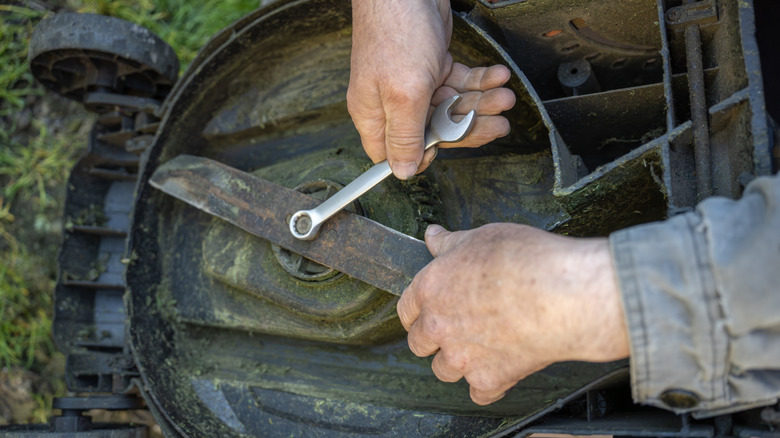 A person removing a lawn mower blade with a wrench