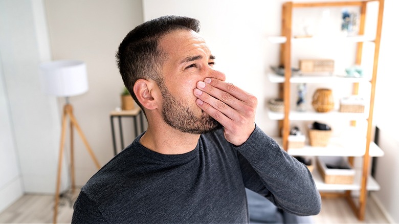 A person holds their nose closed while standing inside a home