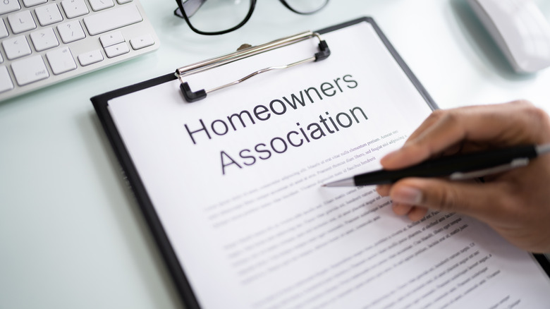 A hand holding a pen over a copy of the homeowner's association guidelines.