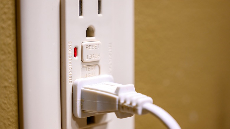 Close-up of the reset button on a GFCI outlet with one power cord plugged in