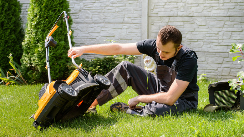 A young man inspecting the underside of a lawn mower