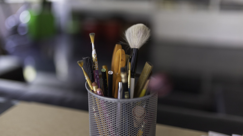 close up of gray pencil holder containing writing utensils and brushes