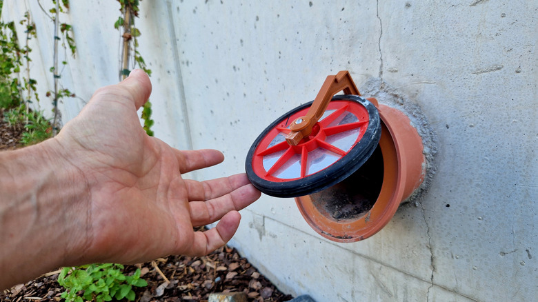 A concrete wall with a drainage pipe covered by a flap to keep out small animals