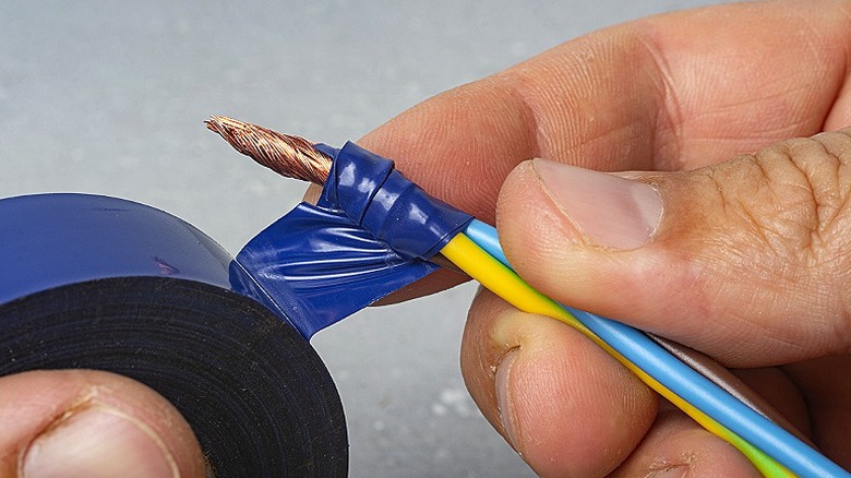 Close-up of a person insulating an electrical wire with electrical tape