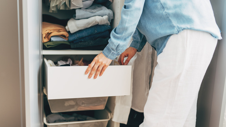 A woman pulling clothing items out of a white bin in her closet