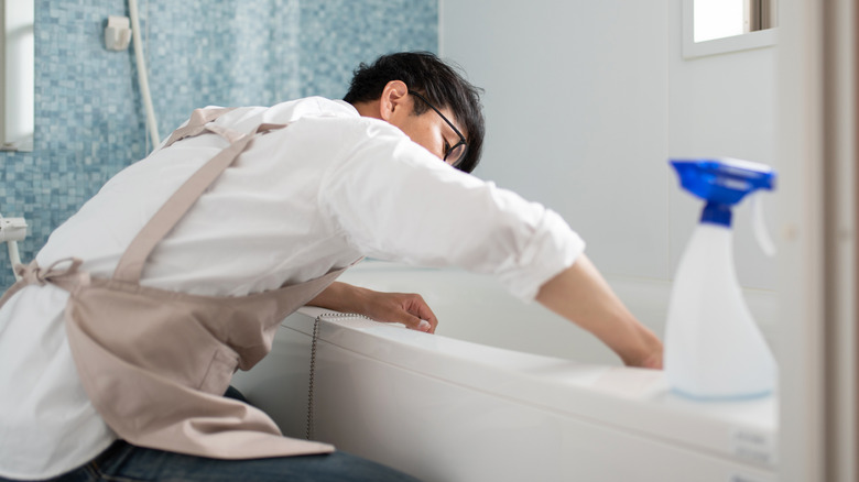 A person cleaning a white bath tub