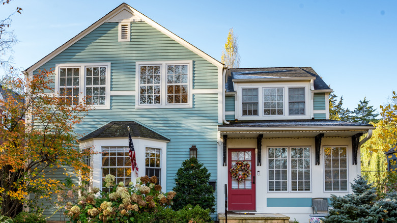 House exterior in fall with trees and flower shrubs in the background