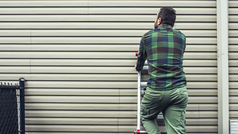 A person on a ladder inspecting the siding on a house