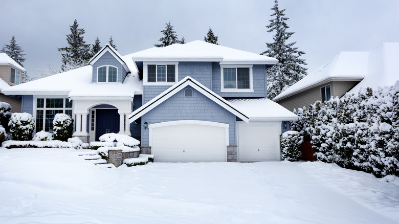 A blue house with white garage with snow around it.
