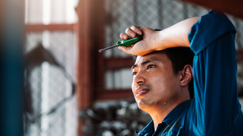 A man holding a screwdriver gets hot in a garage.