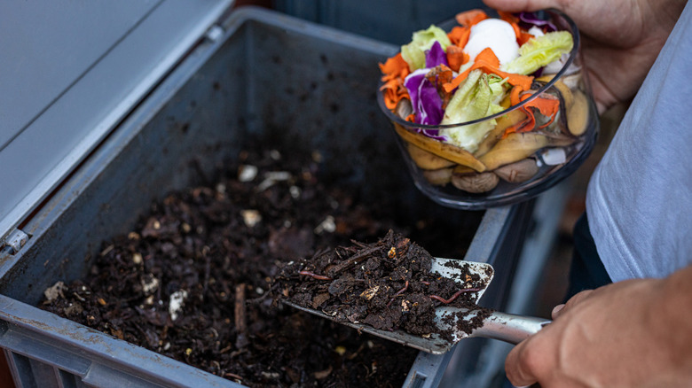 Person adding kitchen scraps to soil in a compost bin