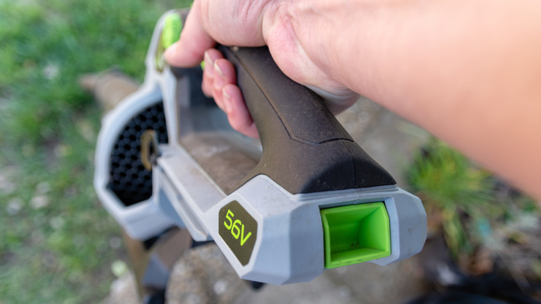 A hand holds a battery-operated leaf blower.