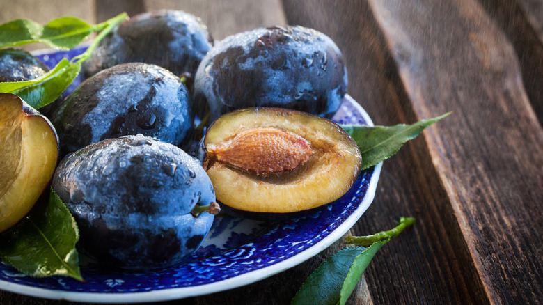 A plate of plums sits on a wooden table