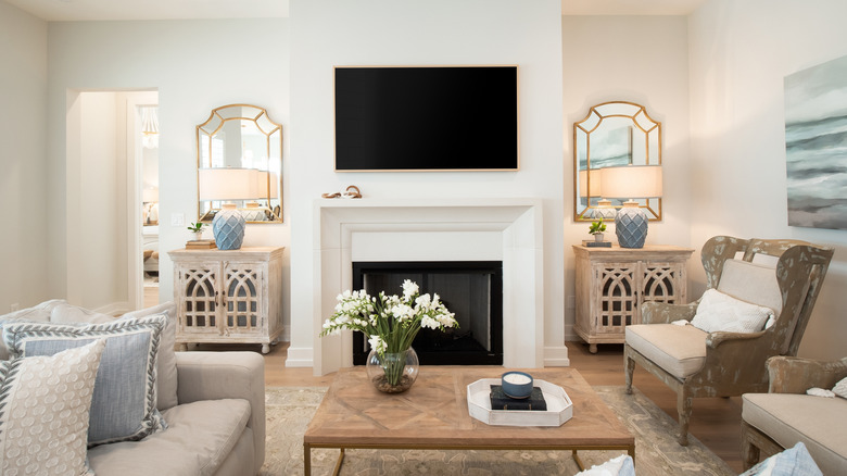 A blue, tan, and white decorated living room with a large TV hanging above a white fireplace