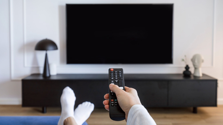 A person holding a remote pointed at a TV mounted above a black table