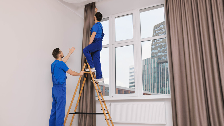 two men in blue clothing hang heavy drapery