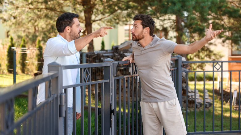 Two frustrated men argue on either side of a wrought iron fence